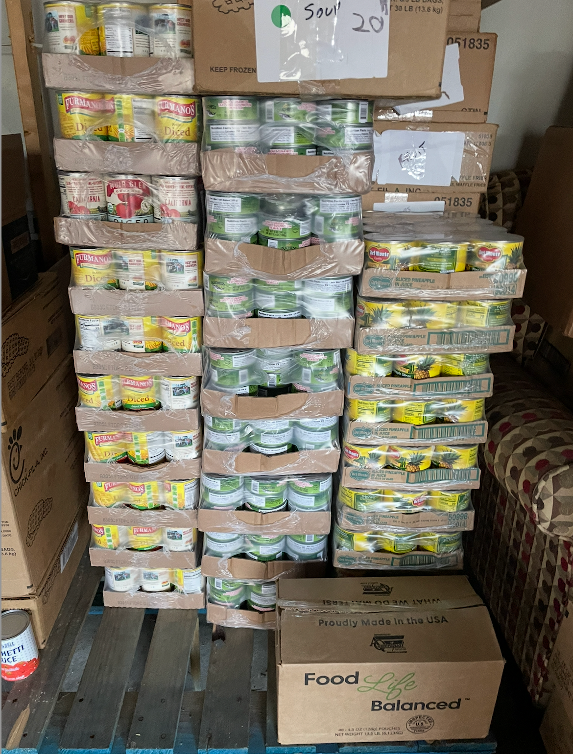 Canned goods stacked on pallets inside a truck. Variety of cans wrapped in plastic. Boxes are labeled.