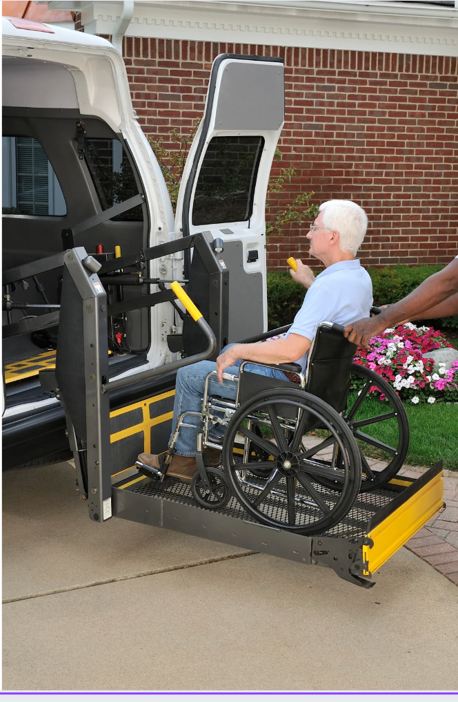 Man in wheelchair using a lift to enter a van. An assistant is beside him.