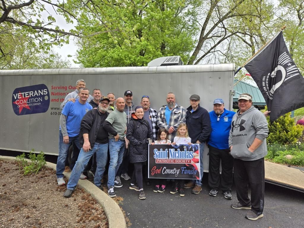 Group of people pose with a banner and a veteran's flag in front of a trailer.