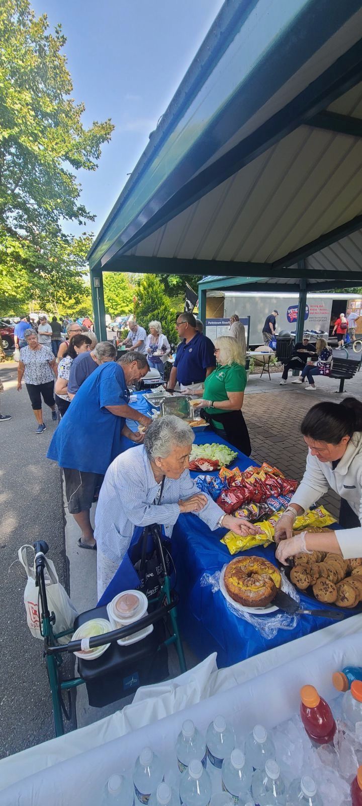 People at an outdoor event with food on tables, under a pavilion.