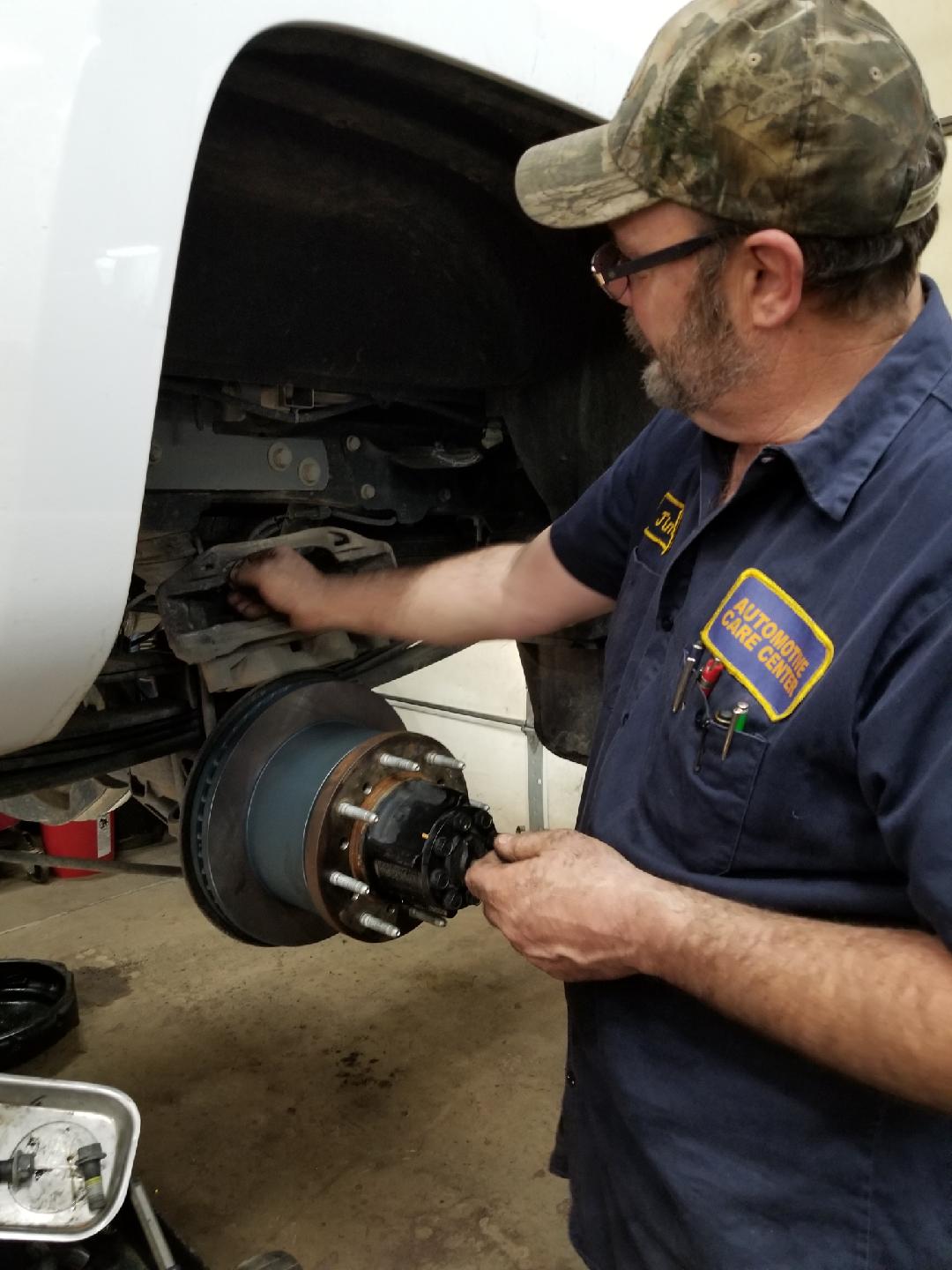 A mechanic in a navy uniform works on the exposed hub and suspension of a vehicle inside a workshop.