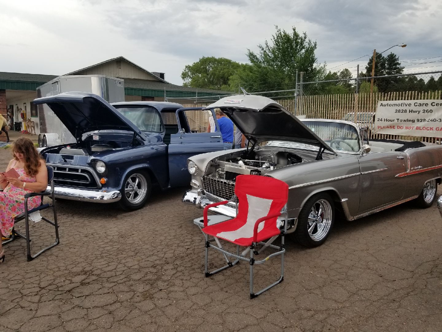 A dark blue pickup truck and a silver convertible parked with hoods open at an outdoor car show, with folding chairs nearby.