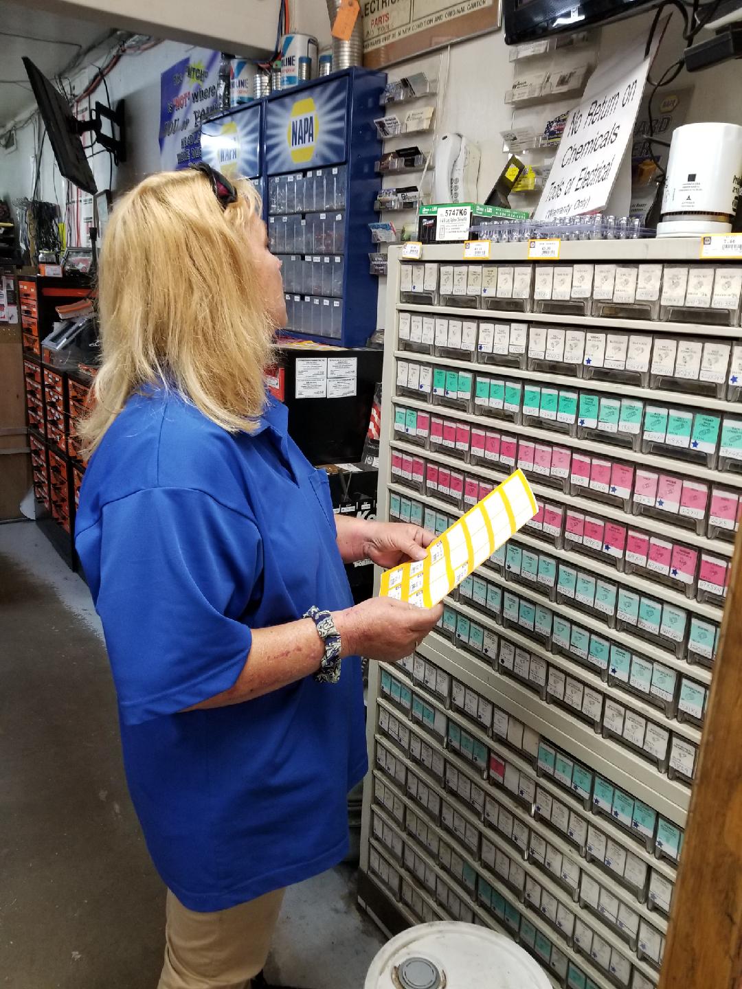 A person in a blue shirt holding a yellow label strip while organizing small parts in a storage bin unit.