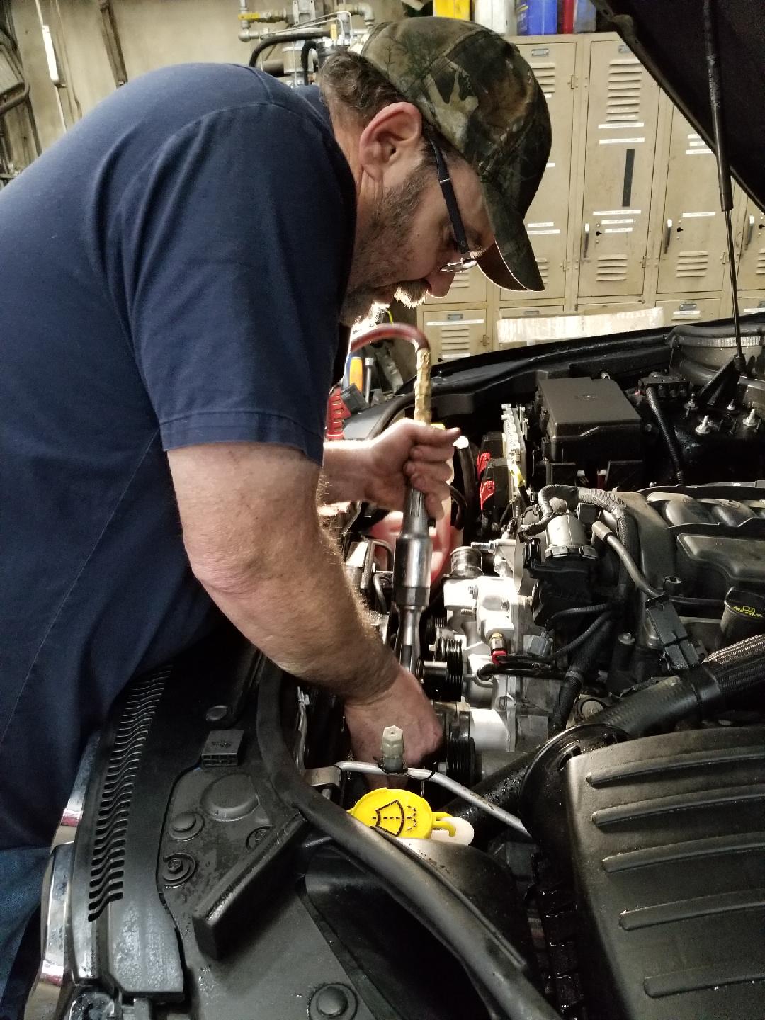 A mechanic in a camo cap works on the engine of a car inside a garage.