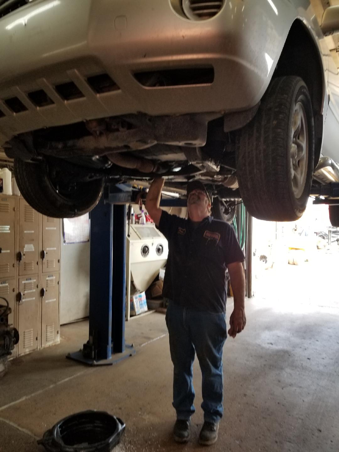 A mechanic working underneath a silver car raised on a hydraulic lift in a garage.