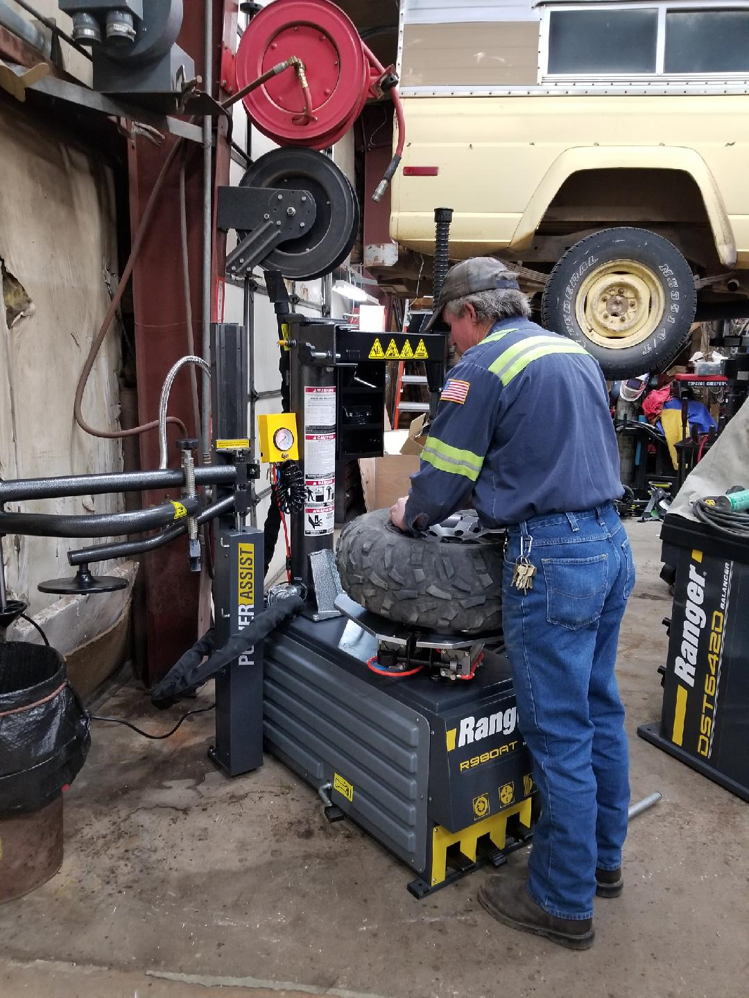 A worker in a blue uniform operates a Ranger tire changer machine in a garage setting.