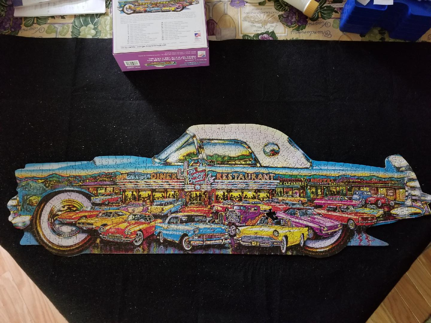 A shaped jigsaw puzzle of a classic car, decorated with an illustration of a retro diner filled with vintage cars.