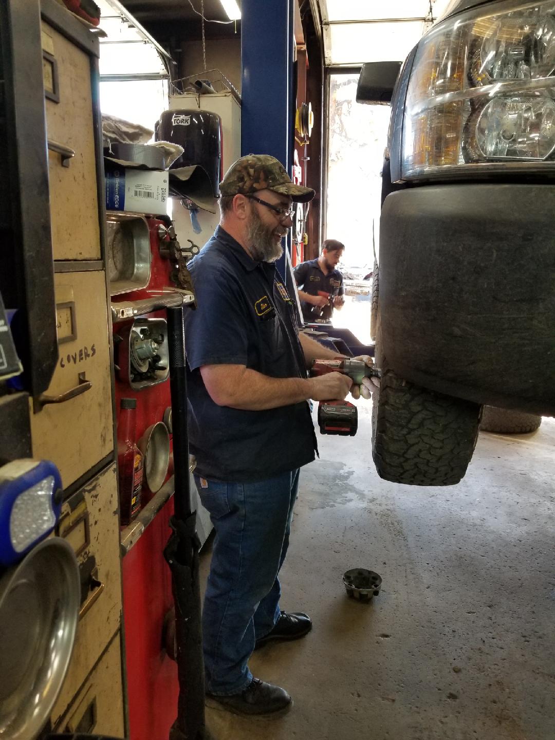 A mechanic using an impact wrench on a tire of a vehicle elevated on a lift inside a workshop.