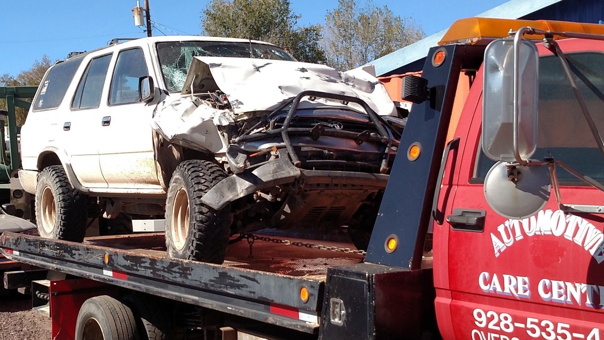 A heavily damaged white SUV loaded onto the flatbed of a red tow truck.