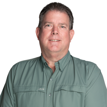 Man in green shirt smiling in front of a tree.