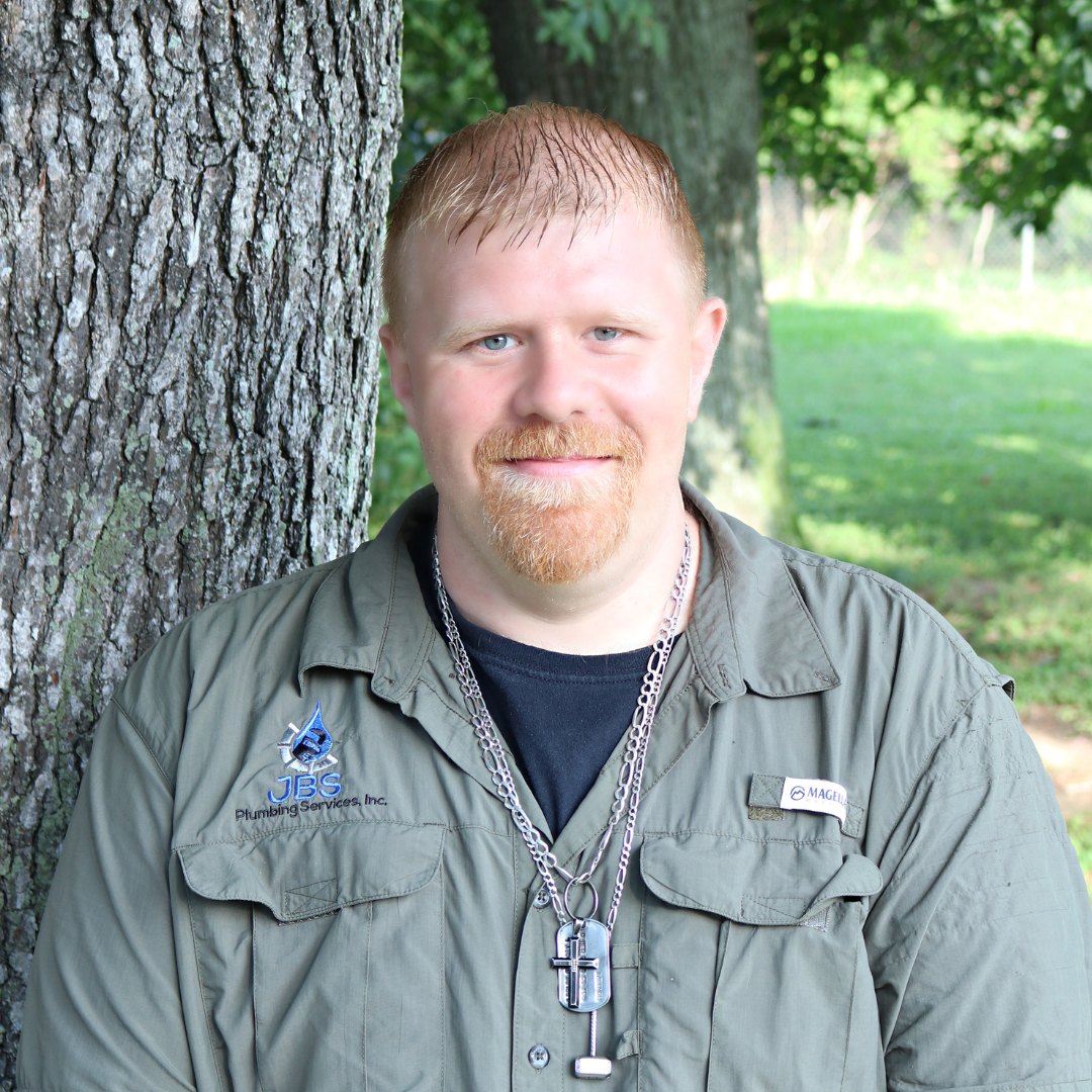 Man with red hair and beard smiling, leaning against a tree in a park.