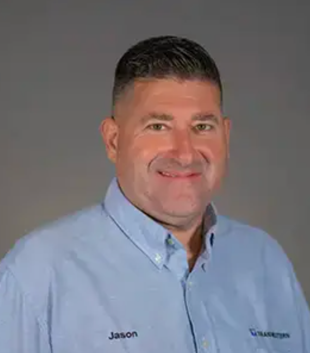 A man named Jason in a blue shirt smiles, set against a gray background.