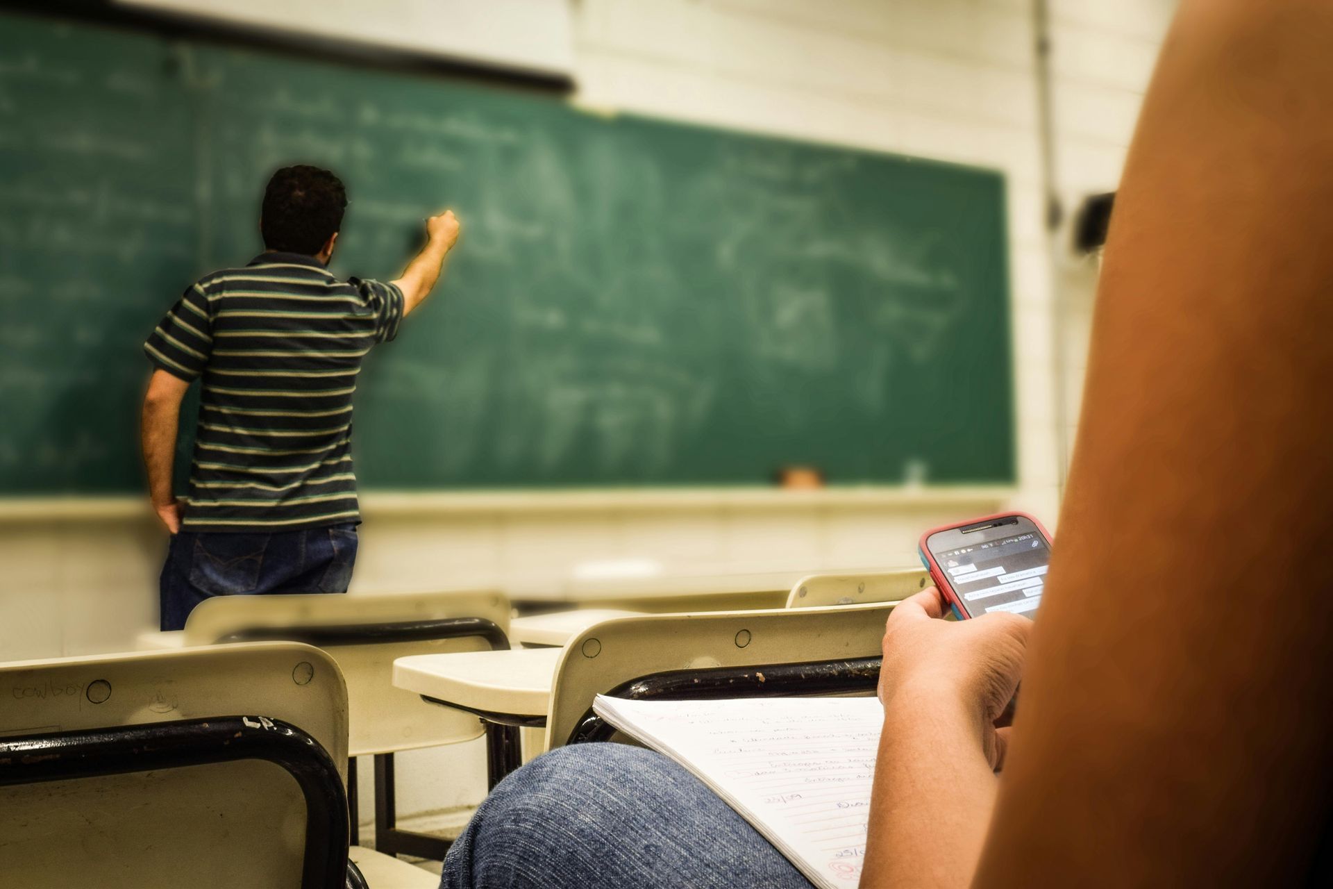 A man is writing on a blackboard in a classroom