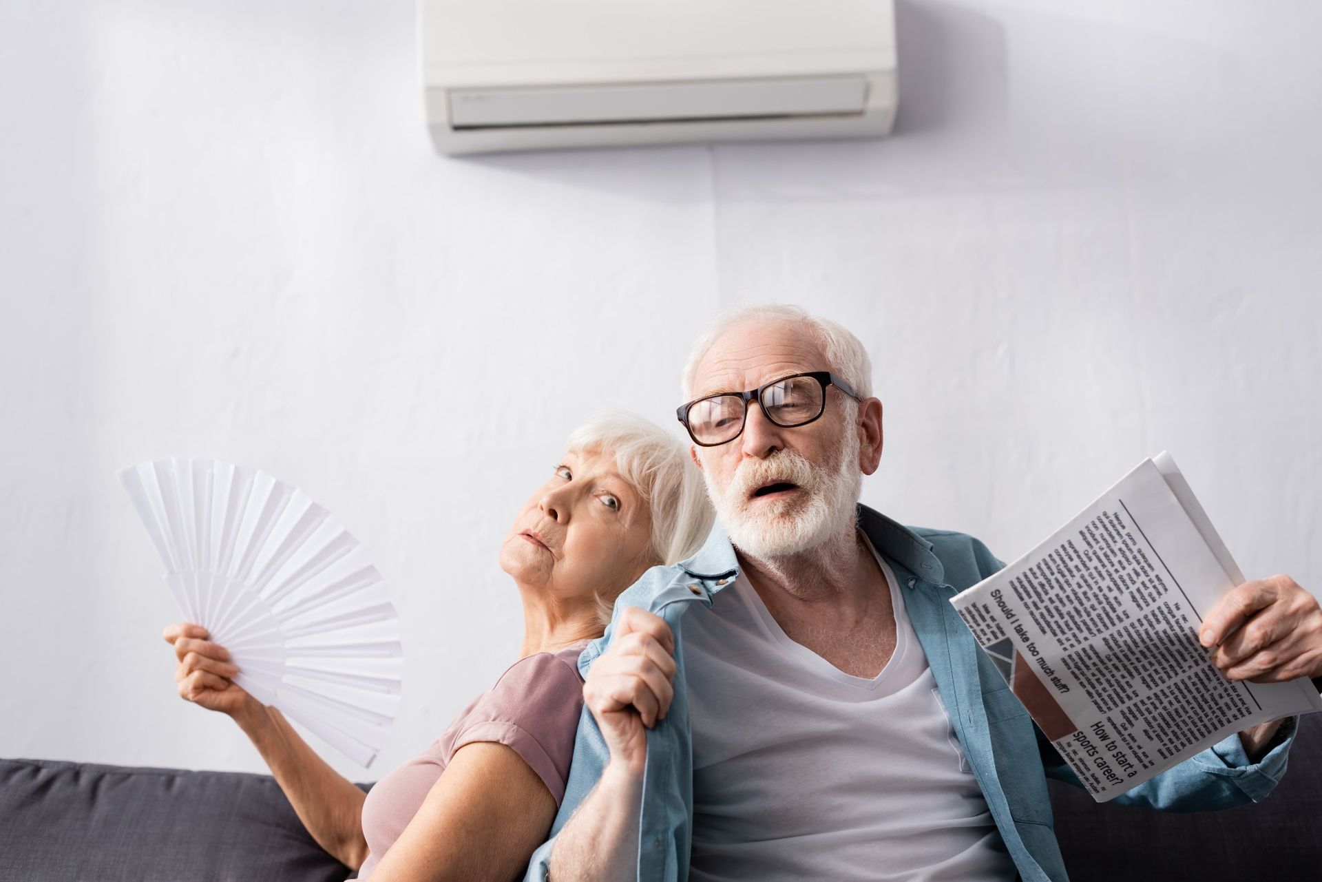 Senior couple feeling hot, humid and uncomfortable indoors while air conditioner runs.