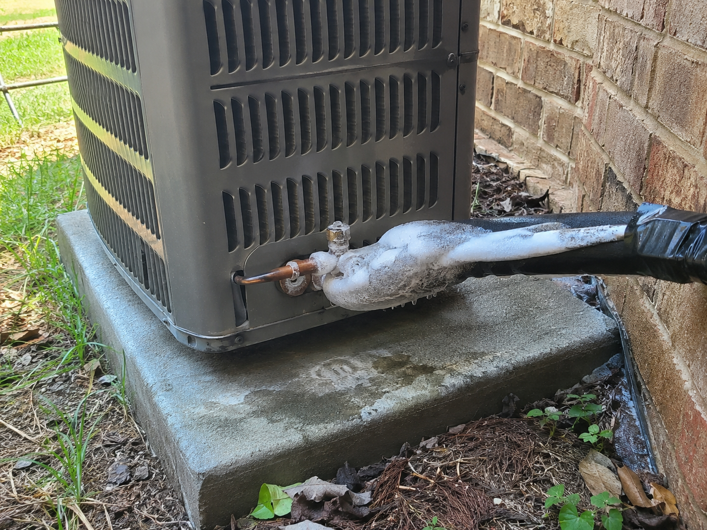 Frozen AC refrigerant line covered in ice beside an outdoor air conditioning unit at a home in Nixa,