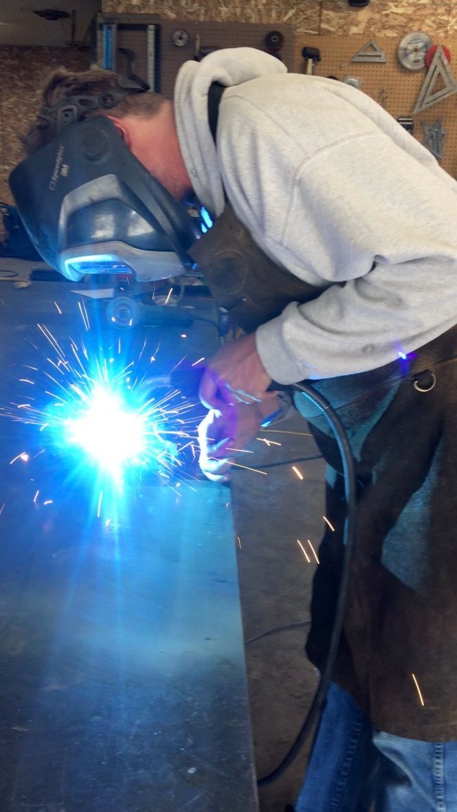 A man wearing a welding mask is welding a piece of metal.