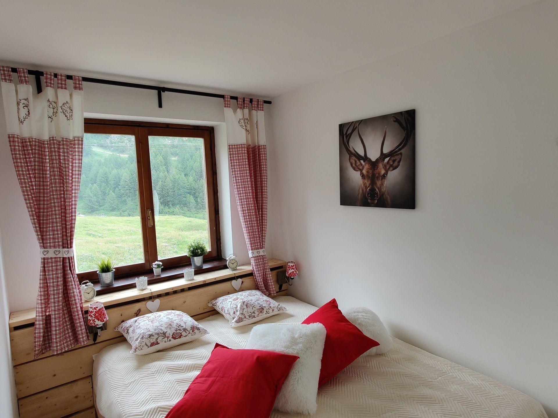 Master bedroom with a double bed with a window behind it. There is a picture on the wall with a deer on it