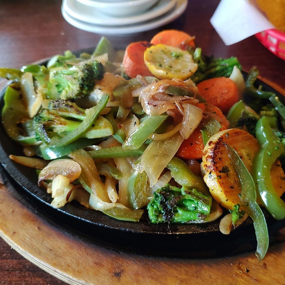 Sizzling mixed vegetables on a black skillet, including broccoli, peppers, onions, and carrots on a wooden board