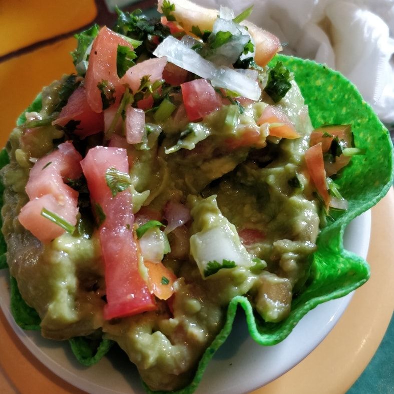 Green tortilla chips topped with guacamole, diced tomatoes, onions, and herbs on a plate