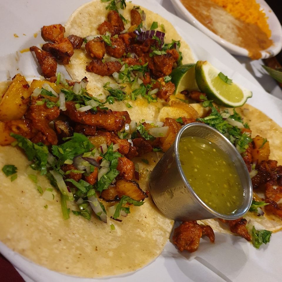 Plated tacos topped with chopped meat, cilantro, onions, lime, and a small cup of green salsa