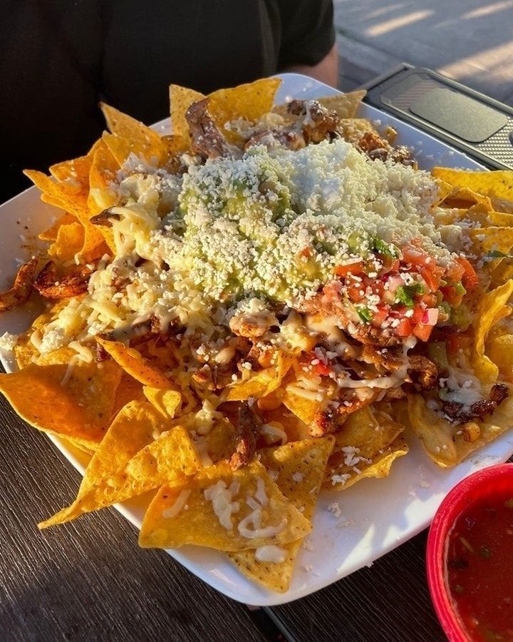 Loaded nachos with cheese, salsa, and guacamole on a white plate with a red dipping cup.