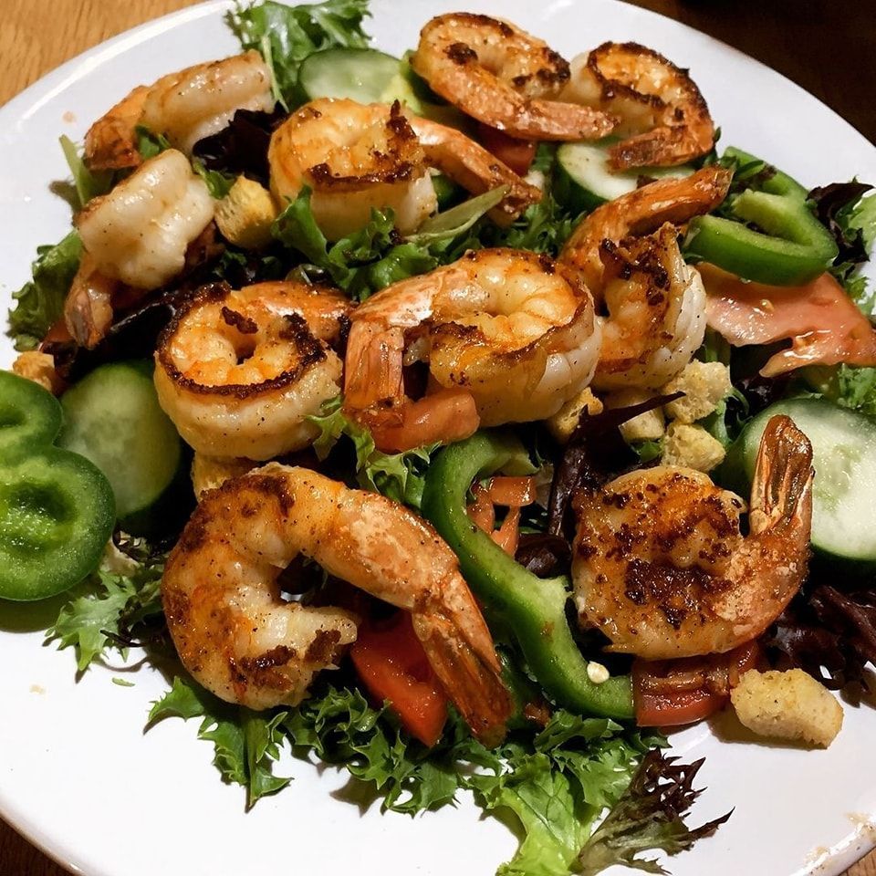 Grilled shrimp salad with cucumber, green peppers, and mixed greens on a white plate