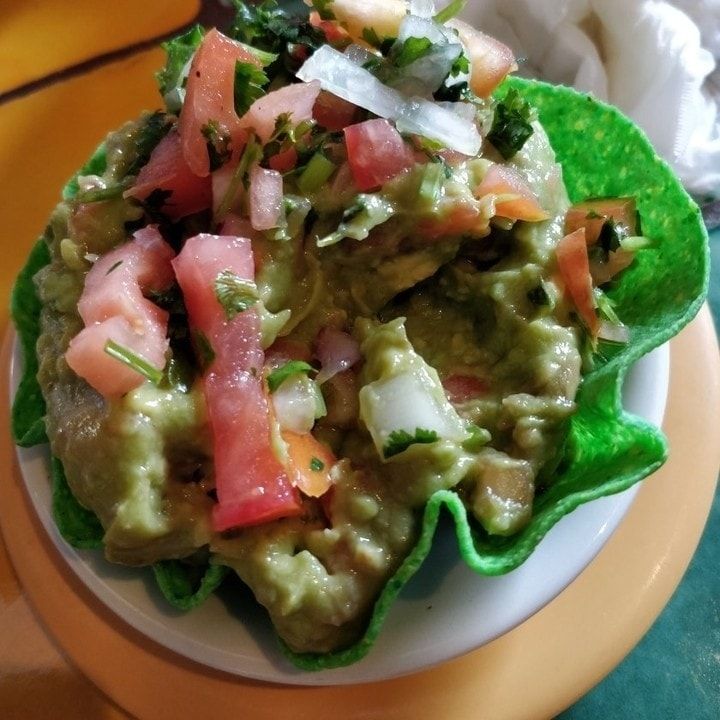 Colorful guacamole in a green tortilla bowl, topped with diced tomatoes and cilantro, on a plate