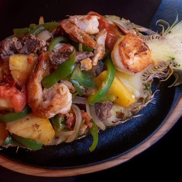 Skillet of shrimp fajitas with peppers, onions, potatoes, and cheese on a dark plate