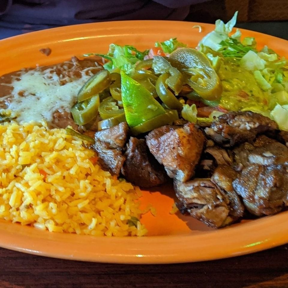 Orange plate with rice, grilled meat, sautéed peppers, and refried beans.