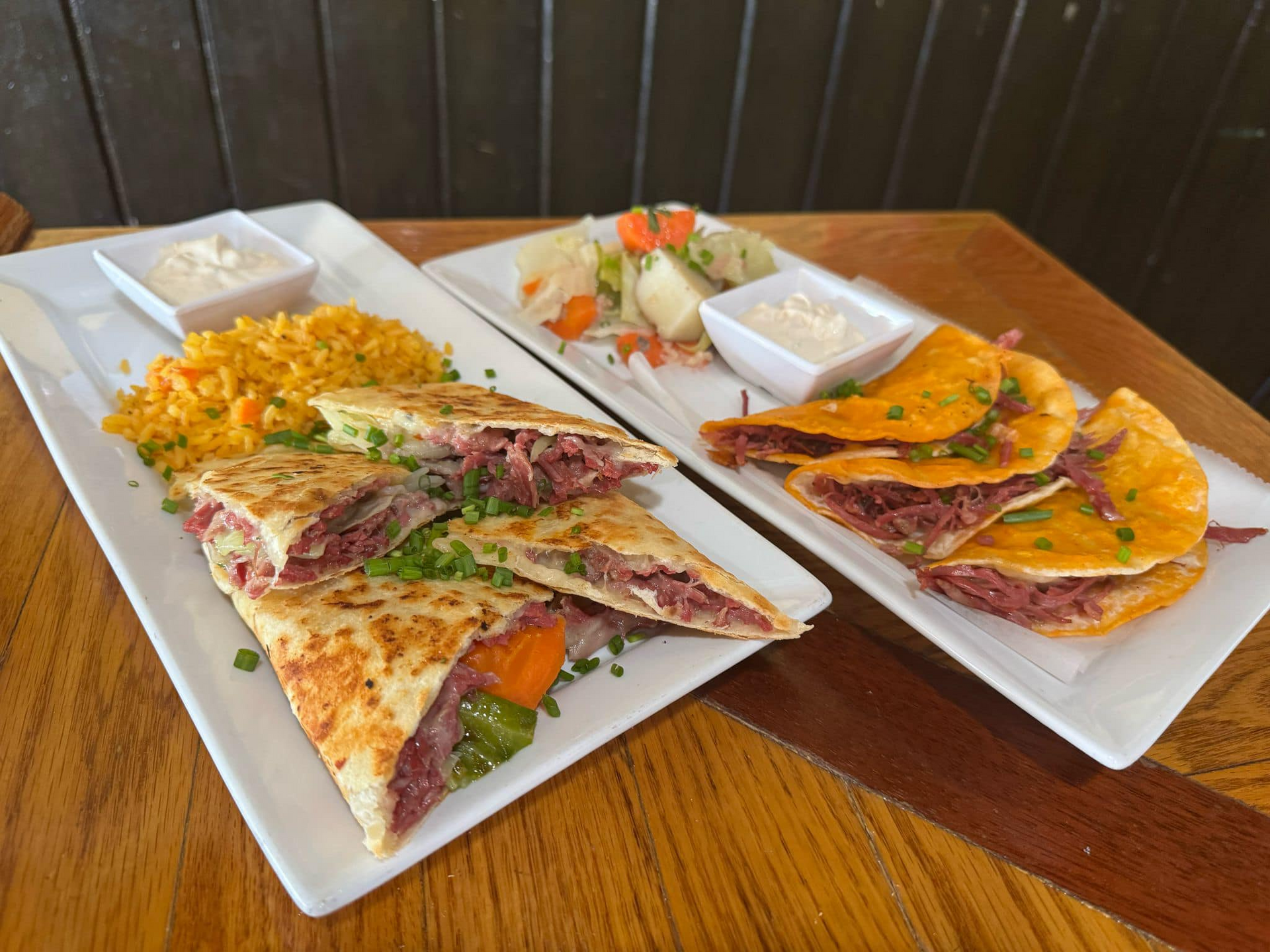Two plates of quesadillas with rice and salsa on a wooden table