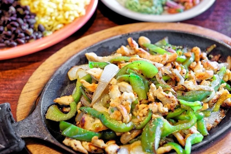 Sizzling stir-fried green peppers and onions with meat on a cast-iron skillet