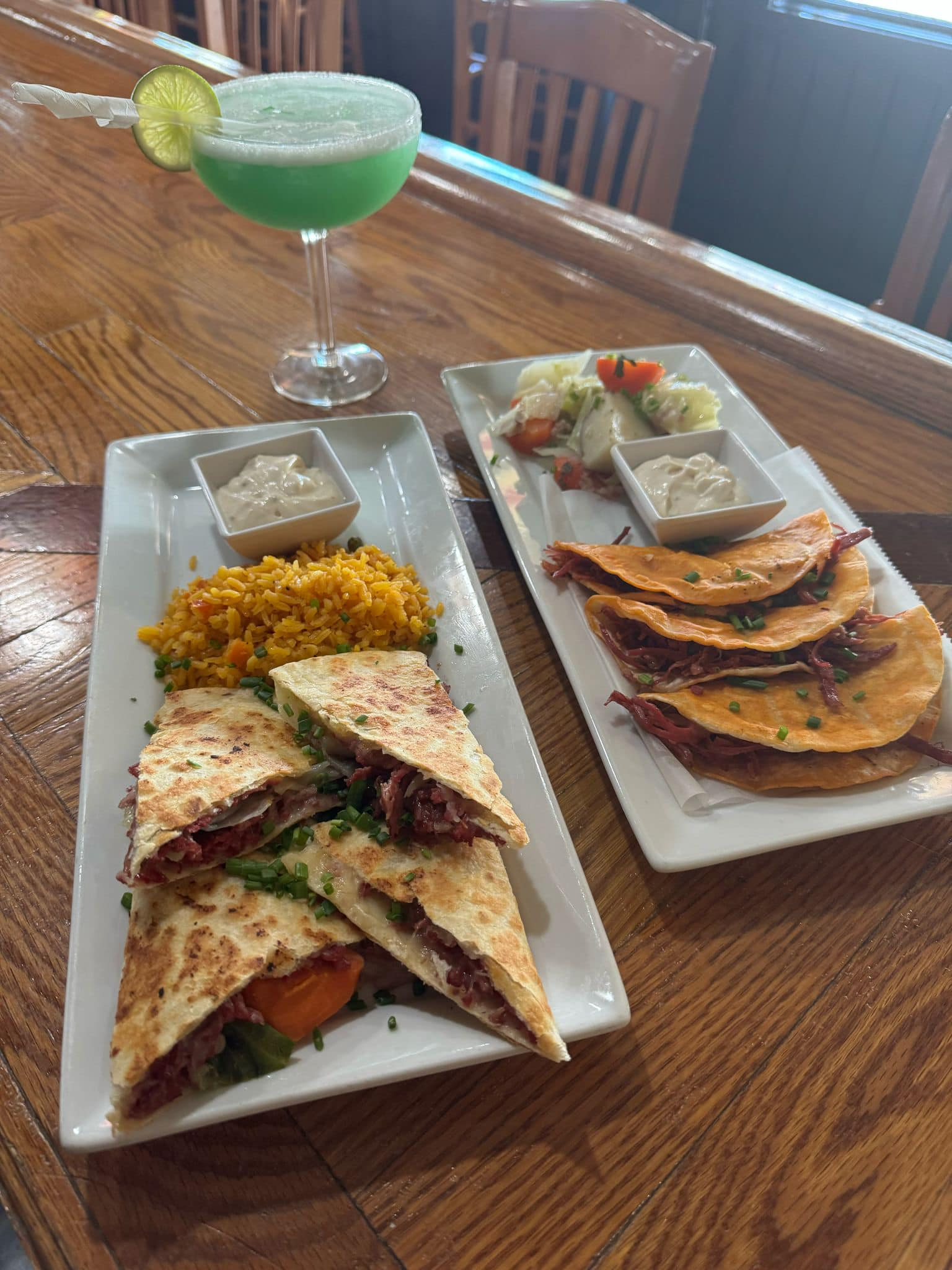 Mexican meal platters with tacos, rice, and green margarita on a wooden table