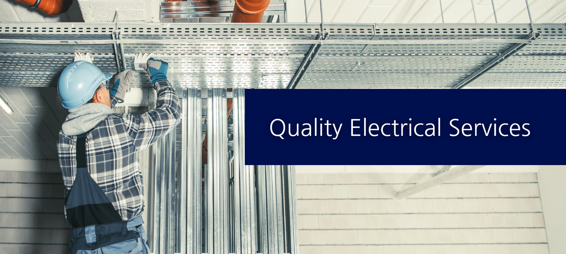 An electrician in a blue hard hat and workwear installs conduit on a metal overhead tray, with 
