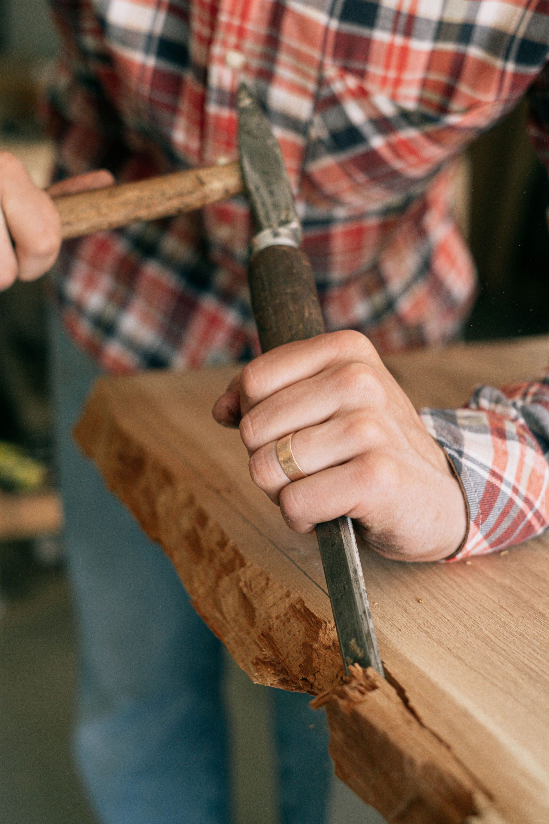 Hands carving wood with a chisel and hammer in order to provide custom carpentry services on a rough table -edge design.