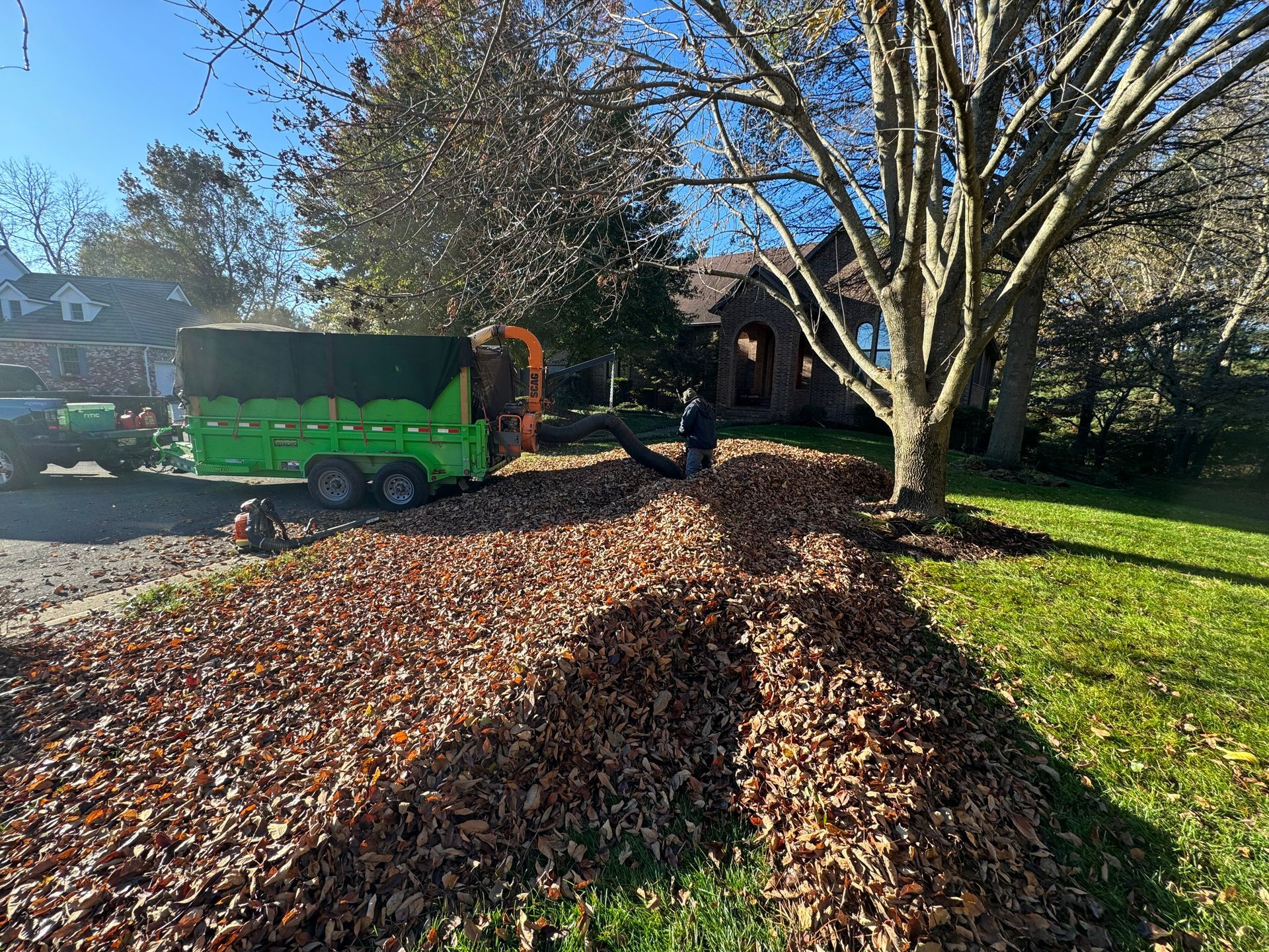 A green trailer is filled with leaves in front of a house.
