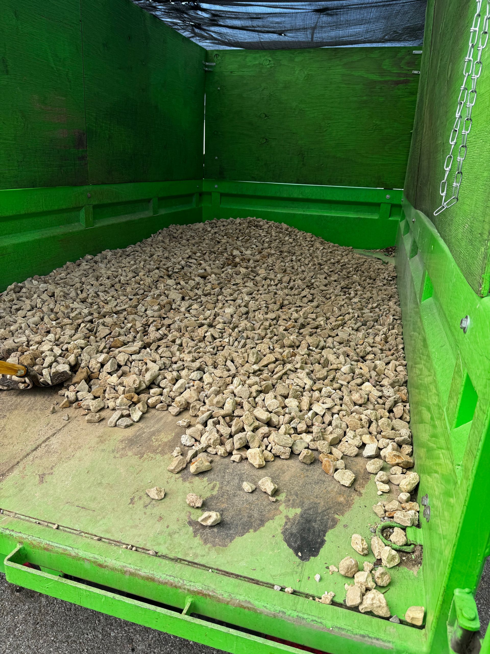 A green dumpster filled with rocks is sitting on the ground.