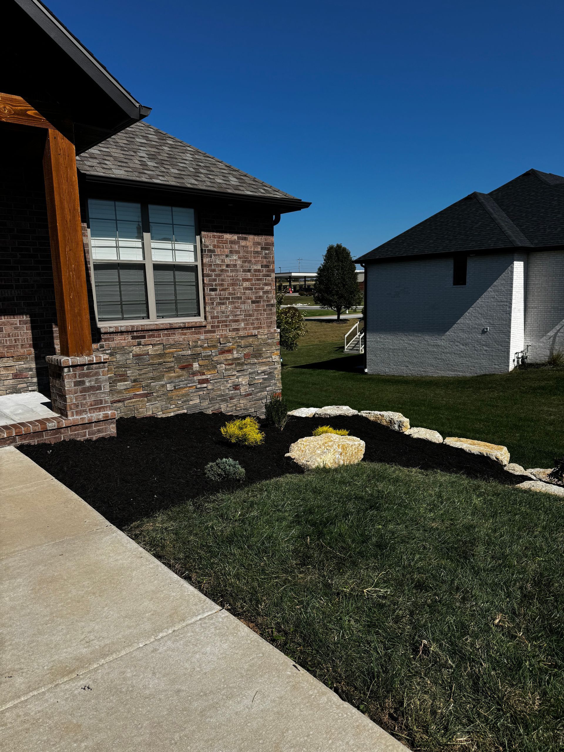 A brick house with a black roof sits next to a white house