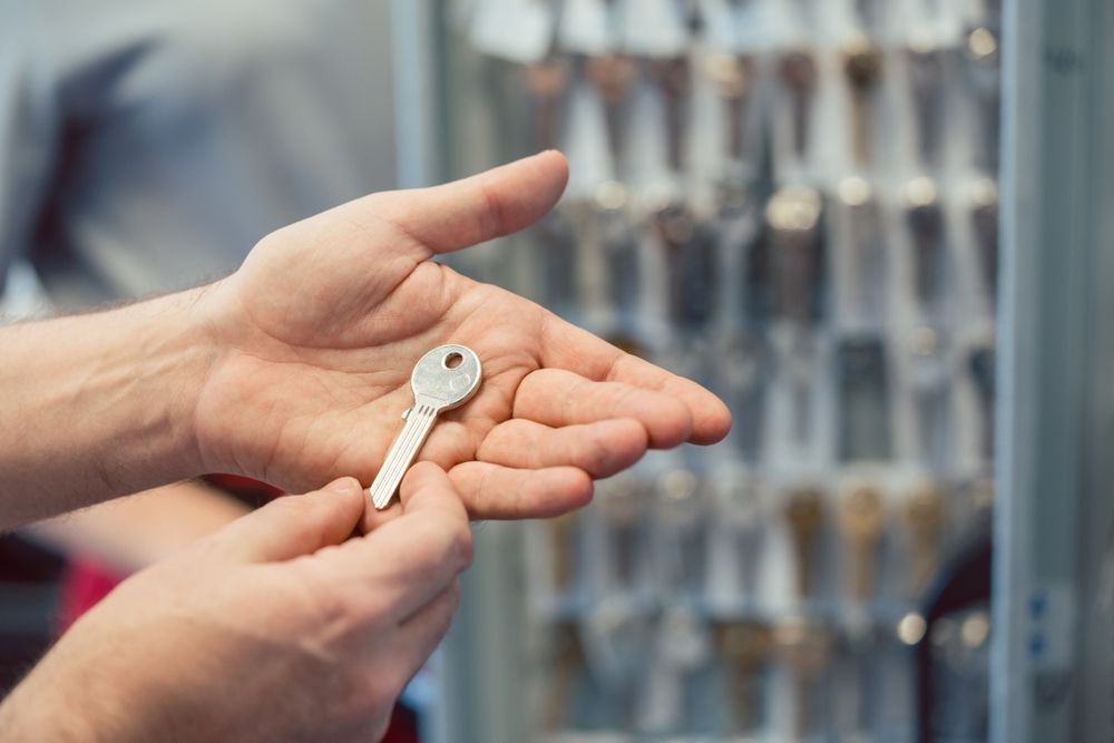 Hands Holding a Silver Key in Front of a Display of Keys — North East Locksmiths in Wodonga, VIC