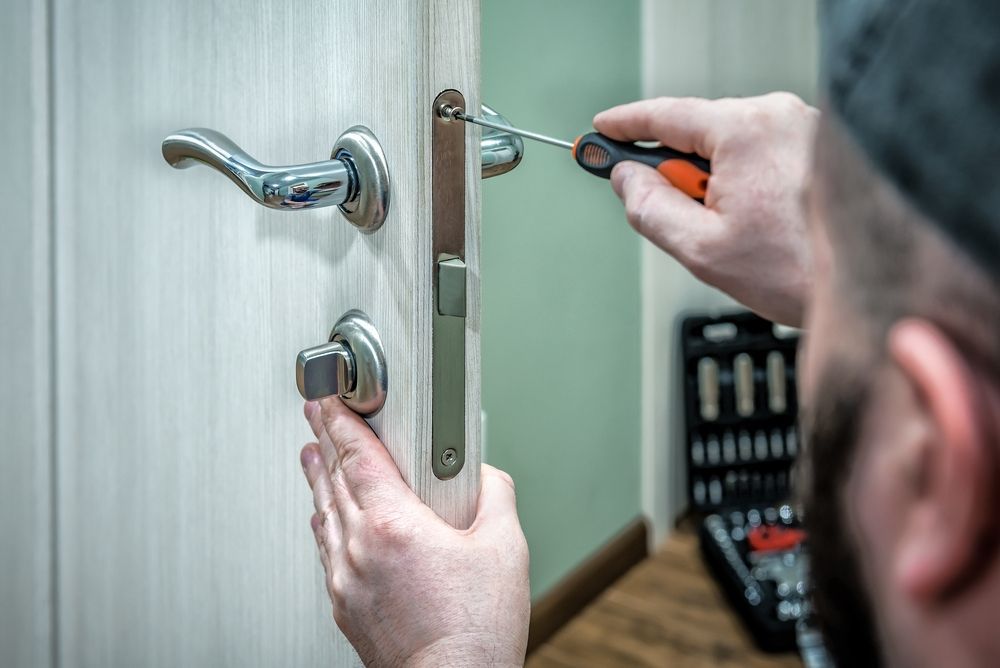 Person Installing a Door Lock With a Screwdriver while Tools on the Floor — North East Locksmiths in Wodonga, VIC