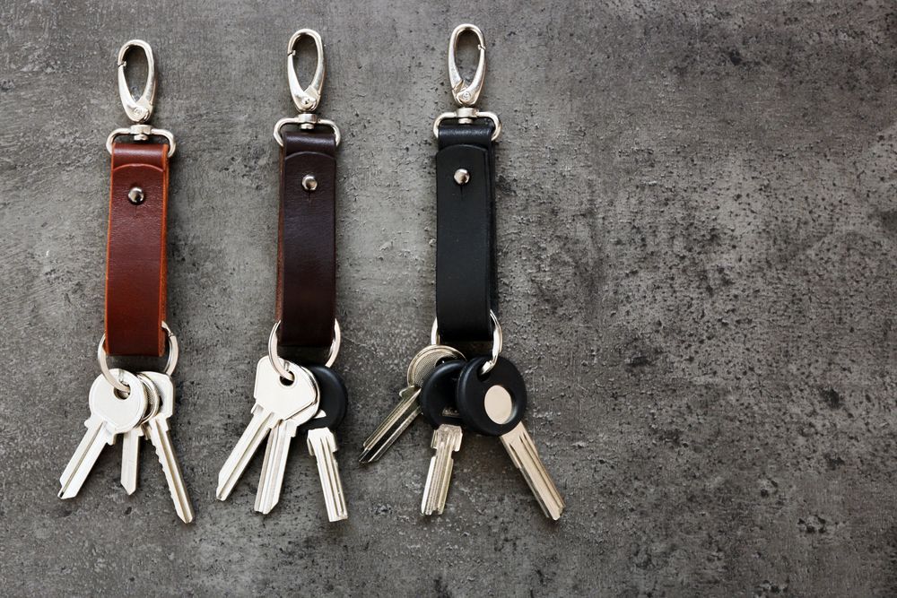 Three Leather Keychains With Silver Clasps and Attached Keys Against a Gray Background — North East Locksmiths in Wodonga, VIC