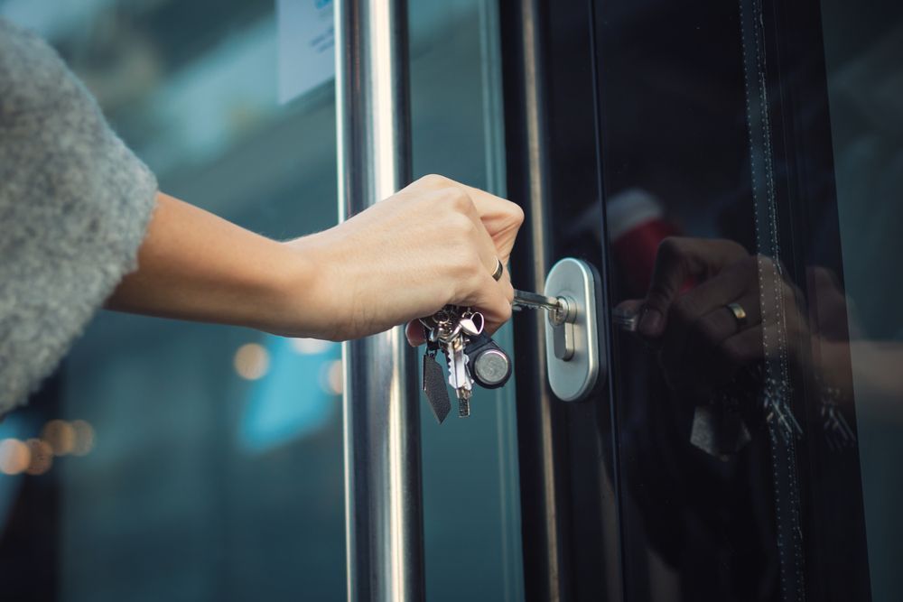 A person's hand unlocking a glass door with a key, holding a small keychain with multiple keys. — North East Locksmiths in Wodonga, VIC
