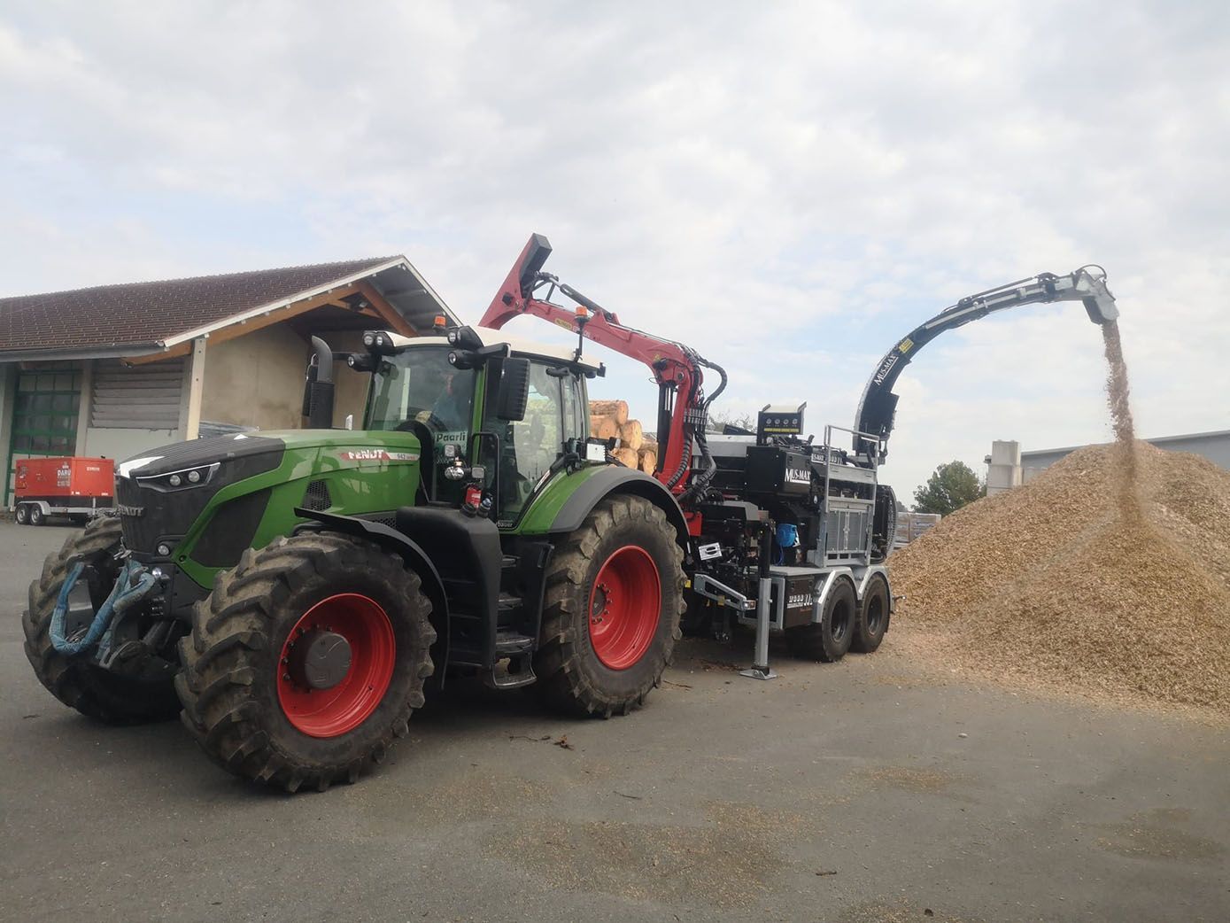 Grüner Traktor mit Holzhäcksler, der Holzspäne auf einen Haufen wirft.
