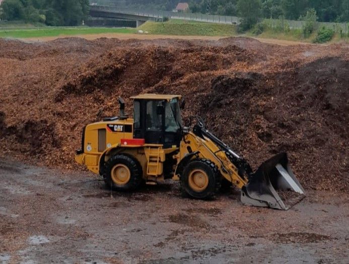 Gelber Caterpillar-Lader, der neben einem großen Haufen Holzspäne geparkt ist.