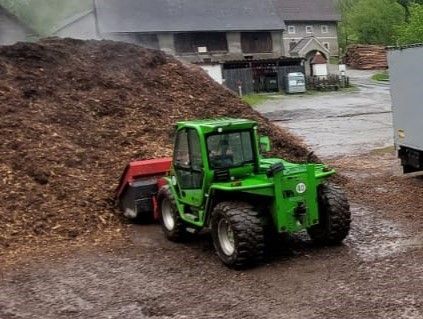 Grüner Traktor lädt Mulch in der Nähe einer Scheune.