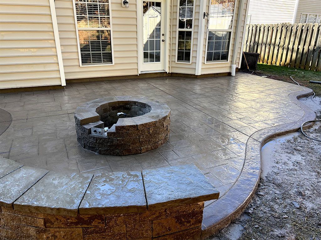Backyard stone patio with a circular fire pit in front of a house with French doors