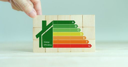 Hand holding an energy efficiency label chart with green-to-red A–G ratings and a house icon
