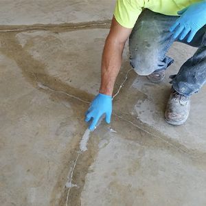 Worker in blue gloves applying sealant to a crack in a concrete floor.