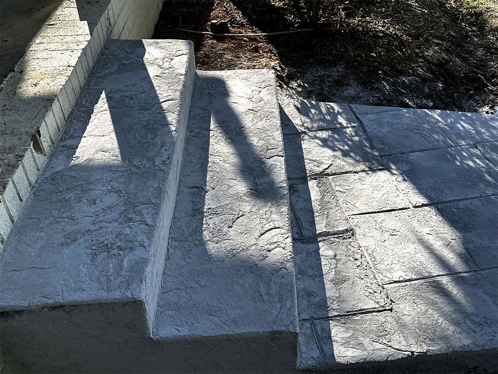 Concrete steps and a ramp in bright sunlight, with long shadows cast across the stone surface.