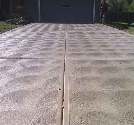 Textured concrete driveway with a central seam leading to a garage, with a person standing at the far right.