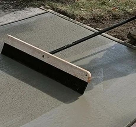 Concrete sidewalk being smoothed with a long-handled finishing tool during repair work